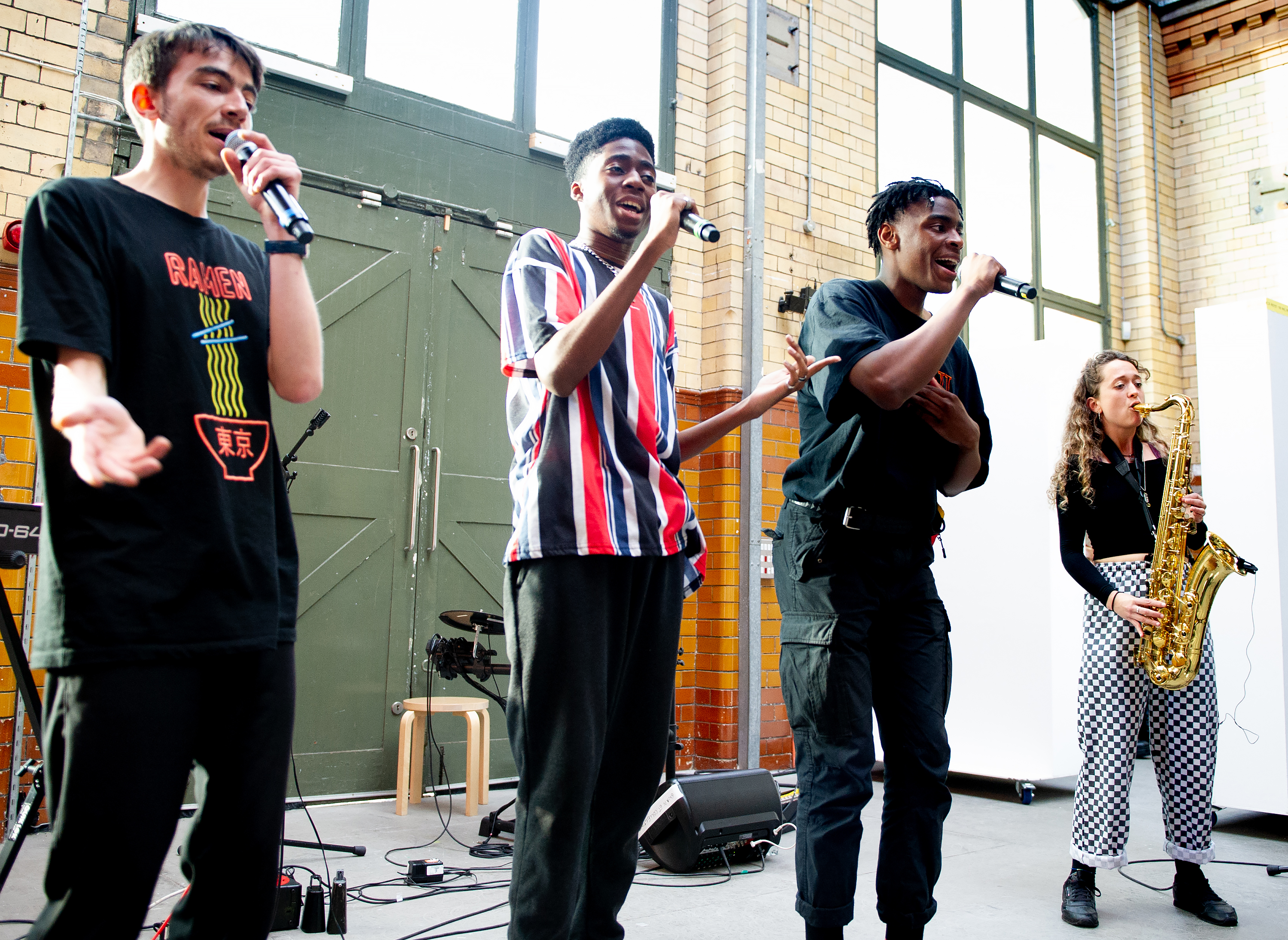Four DISRUPT participants. The three on the left  - Asriel, Kin Louie and DAYZY - are all singing into microphones. Emily Kiely on the far right is playing saxophone.