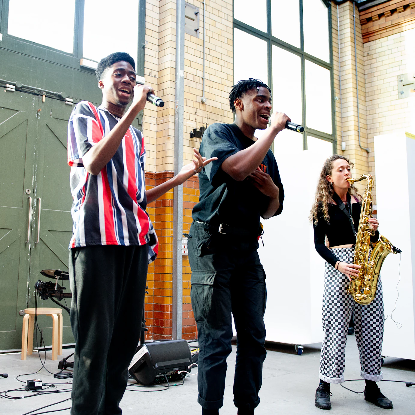 Four DISRUPT participants. The three on the left - Asriel, Kin Louie and DAYZY - are all singing into microphones. Emily Kiely on the far right is playing saxophone.