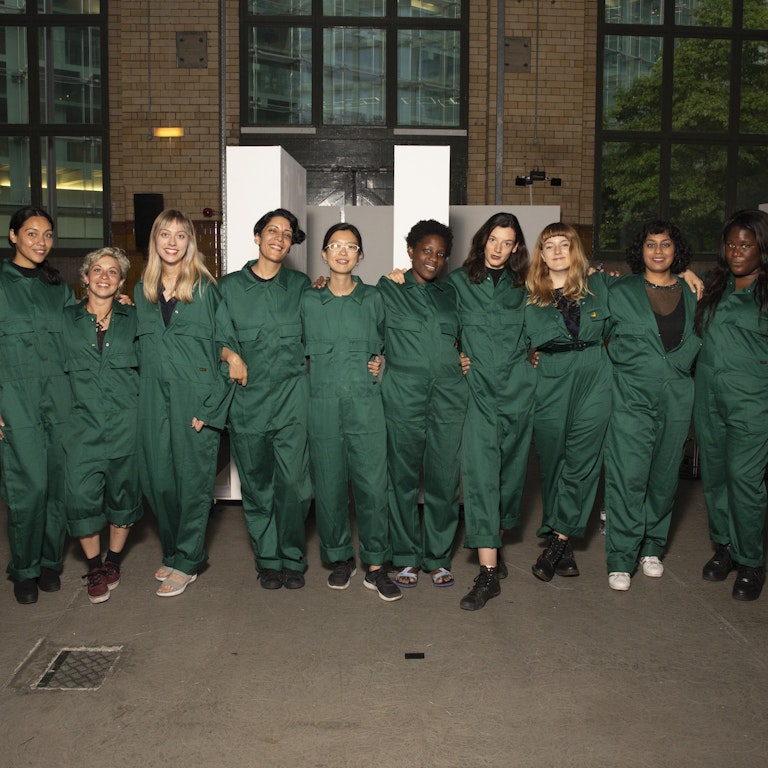 Residency artists, Fatima Al Qadiri and Amal Khalaf stood in a row together for a photo. They're all dressed in dark green boiler suits.