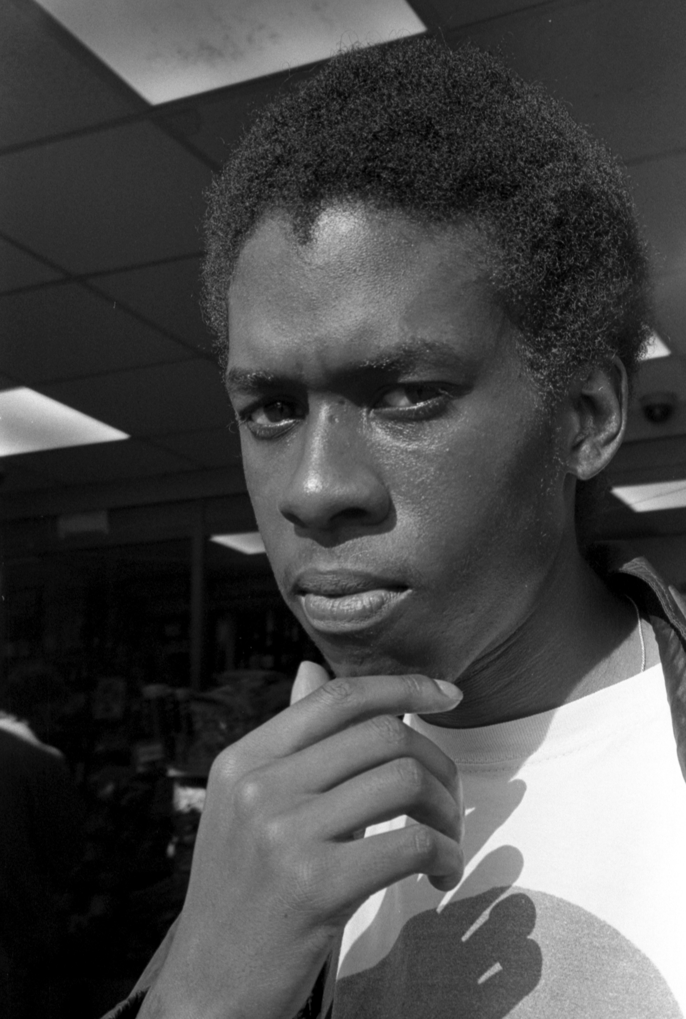 A close-up black and white image of Isaiah Hull looking directly into the camera with his hand touching his chin.