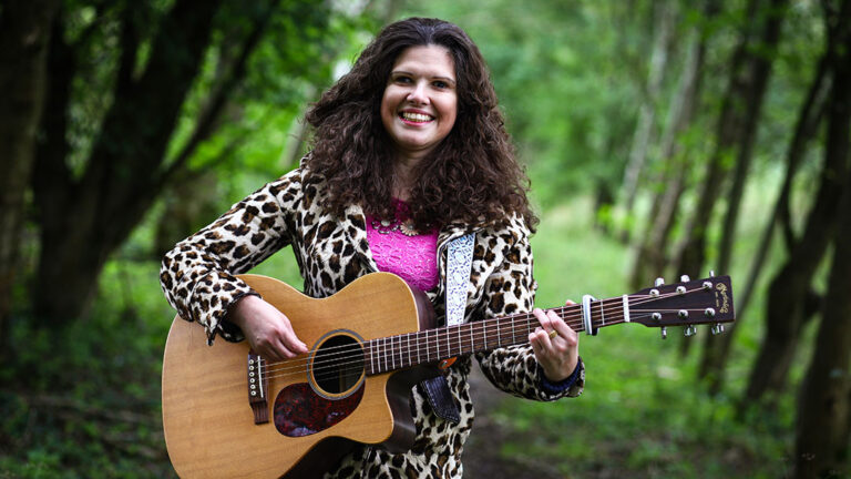Elena Piras stood in woodland playing a guitar and smiling into the camera.