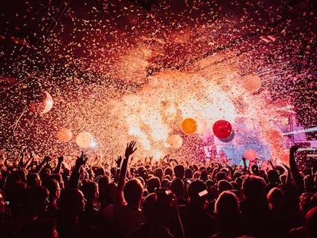 A large audience at a Flaming Lips concert at the Manchester Academy. Confetti, balloons and smoke fill the air. A lot of people have their hands in the air.