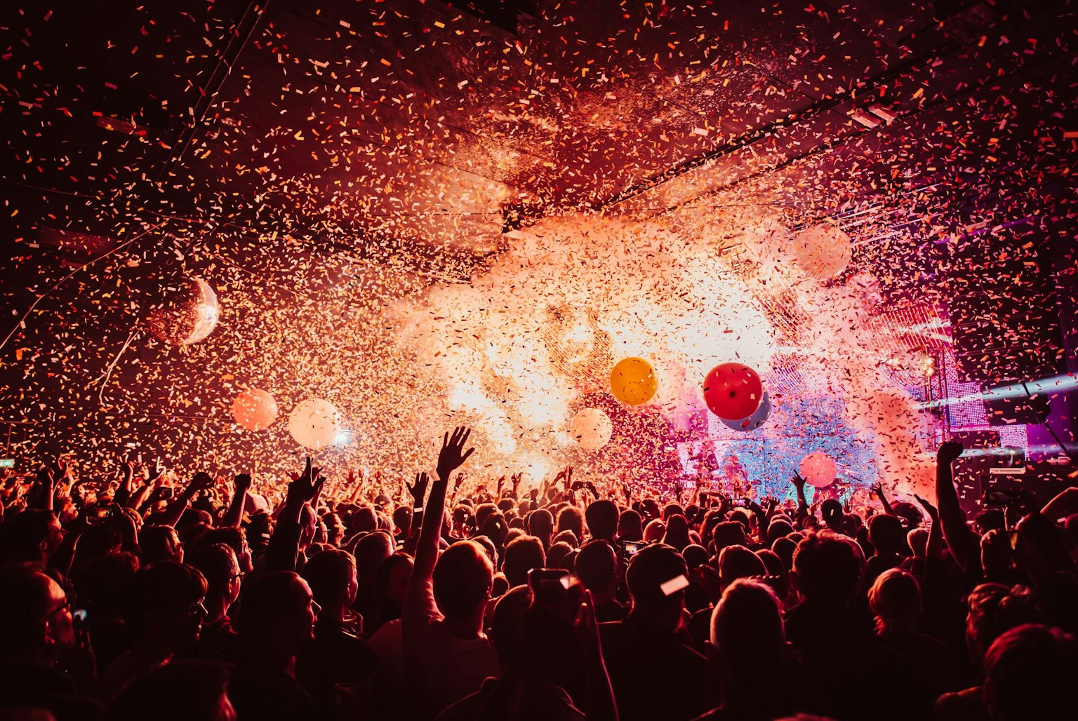 A large audience at a Flaming Lips concert at the Manchester Academy. Confetti, balloons and smoke fill the air. A lot of people have their hands in the air.