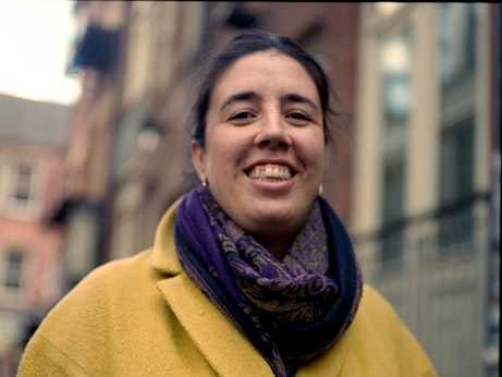 Issy smiles at the camera whilst wearing a yellow coat and purple patterned scarf. 