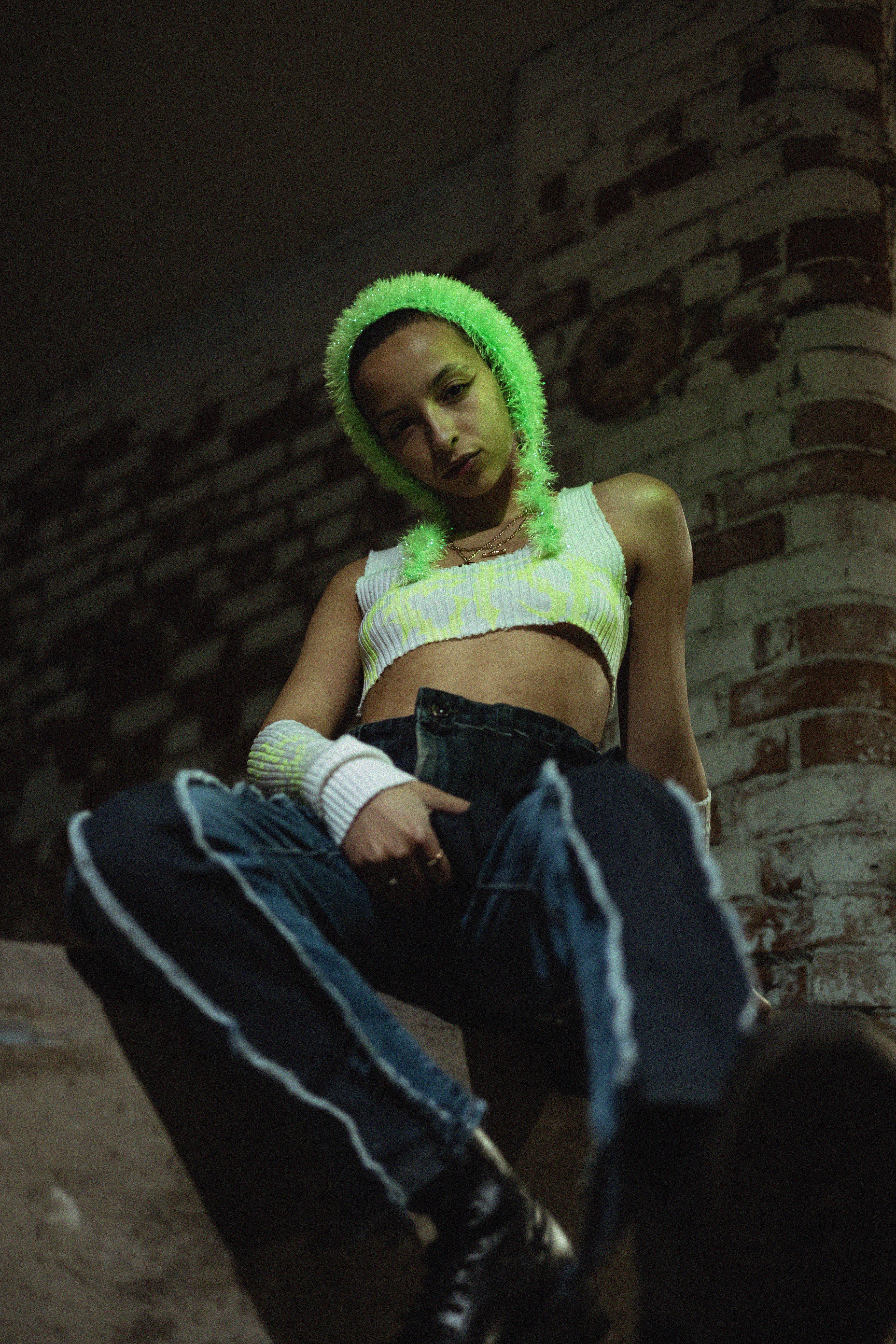 Karis Jade sat on a ledge with a brick structure behind her looking down into the camera.