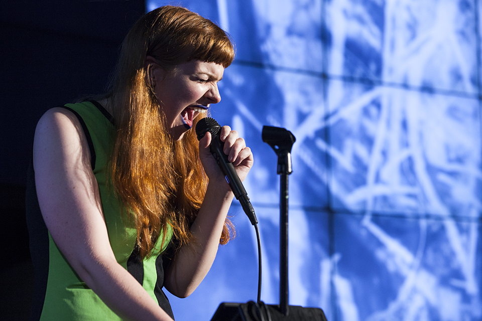 A musician singing into a microphone in front of projected visuals.