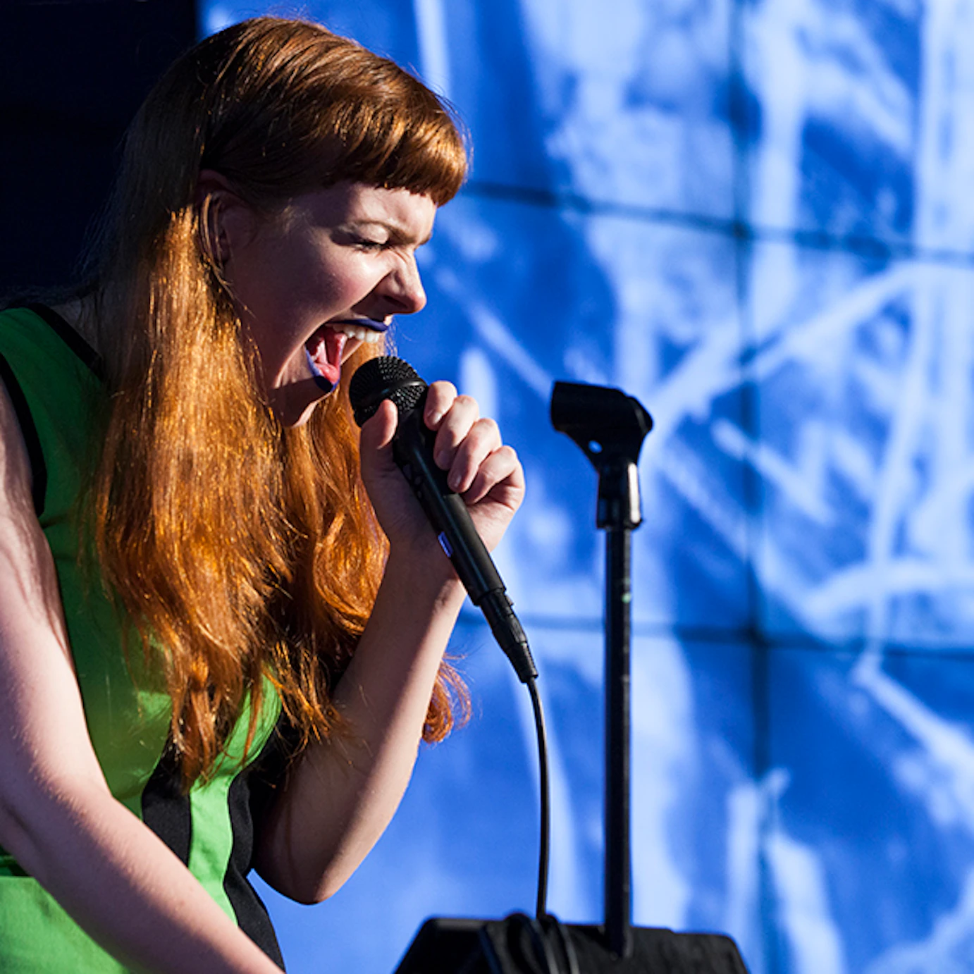 A musician singing into a microphone in front of projected visuals.