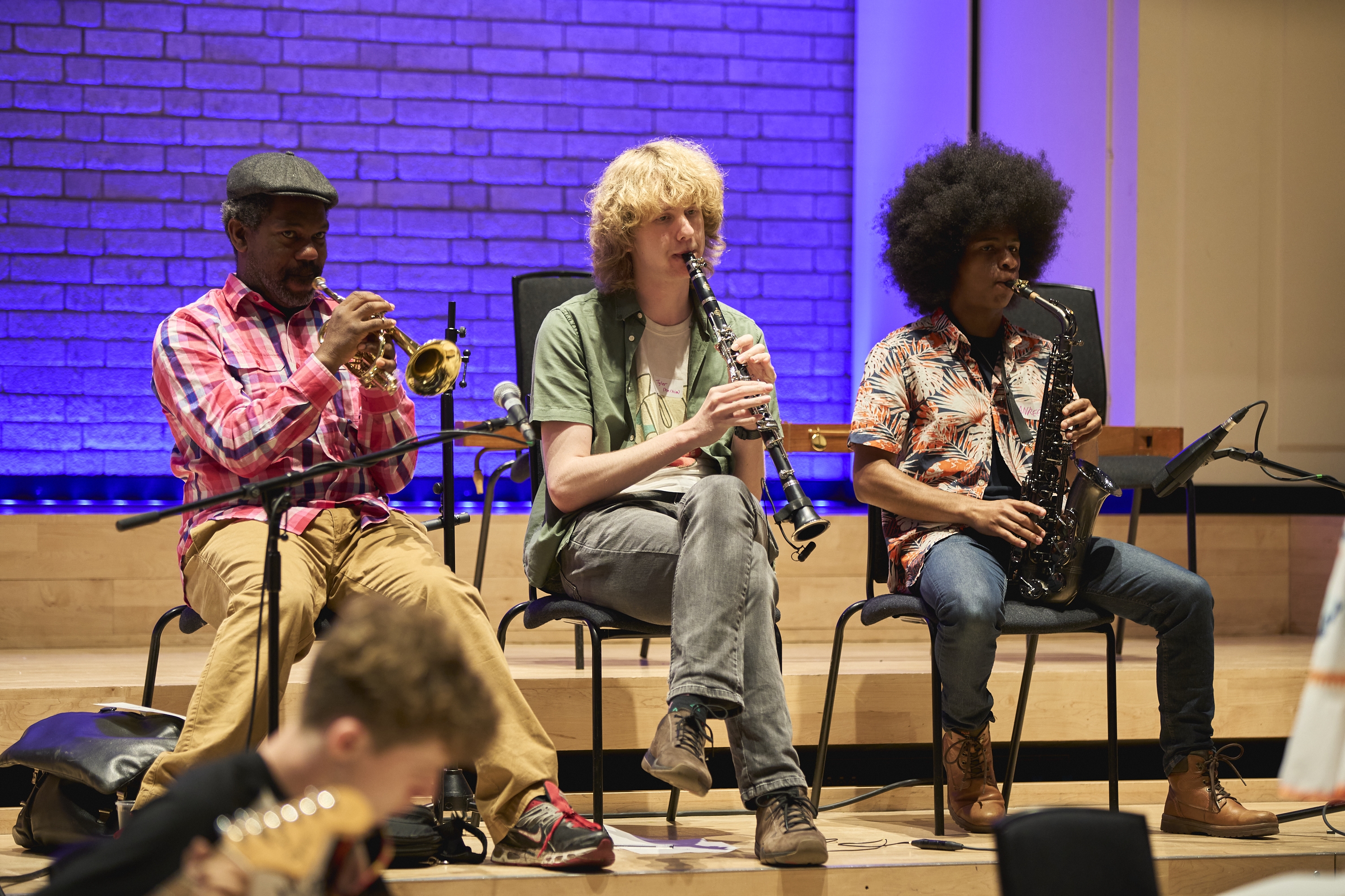 Bryon Wallen and two young musicians sat in a row playing a trumpet, clarinet and saxophone respectively.