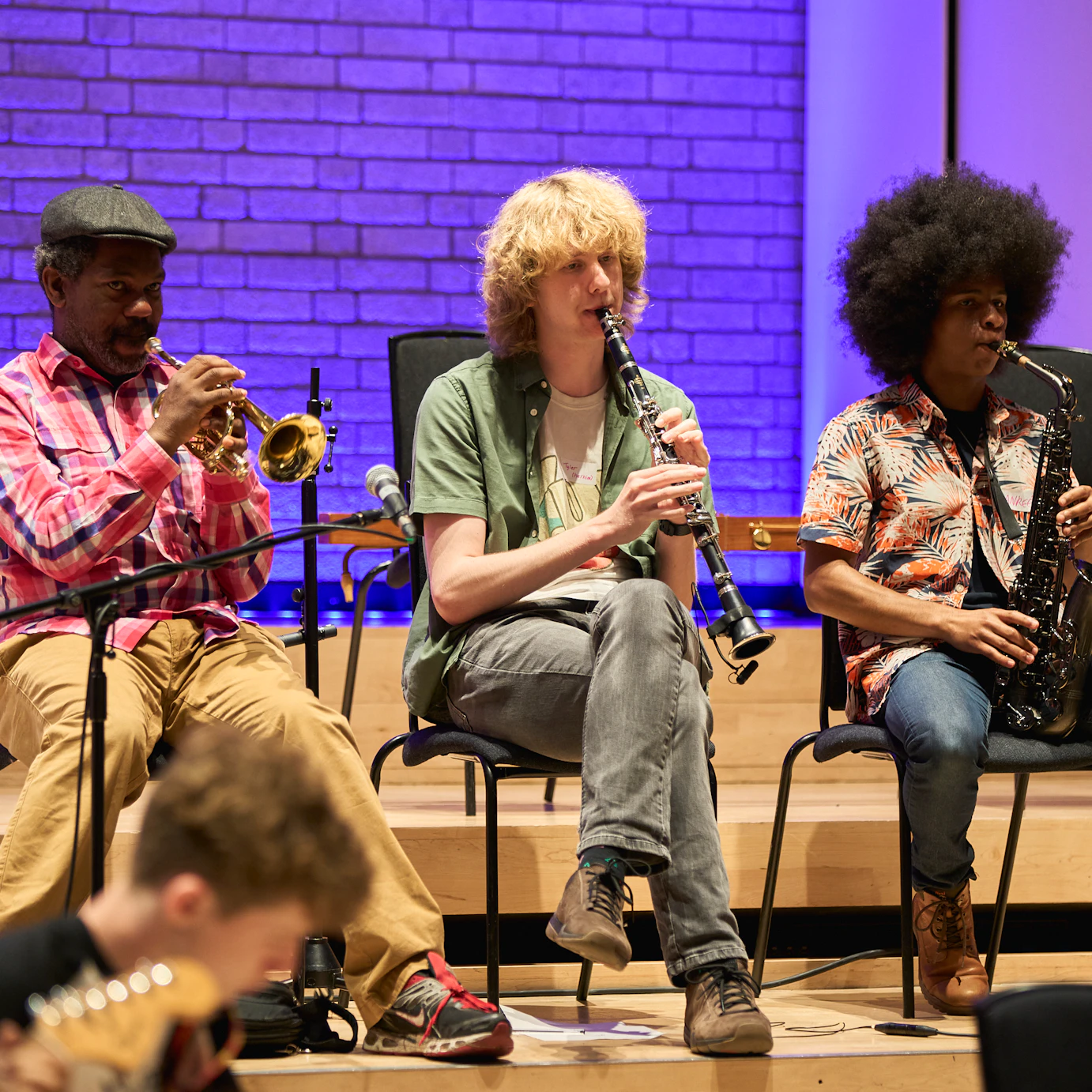 Bryon Wallen and two young musicians sat in a row playing a trumpet, clarinet and saxophone respectively.