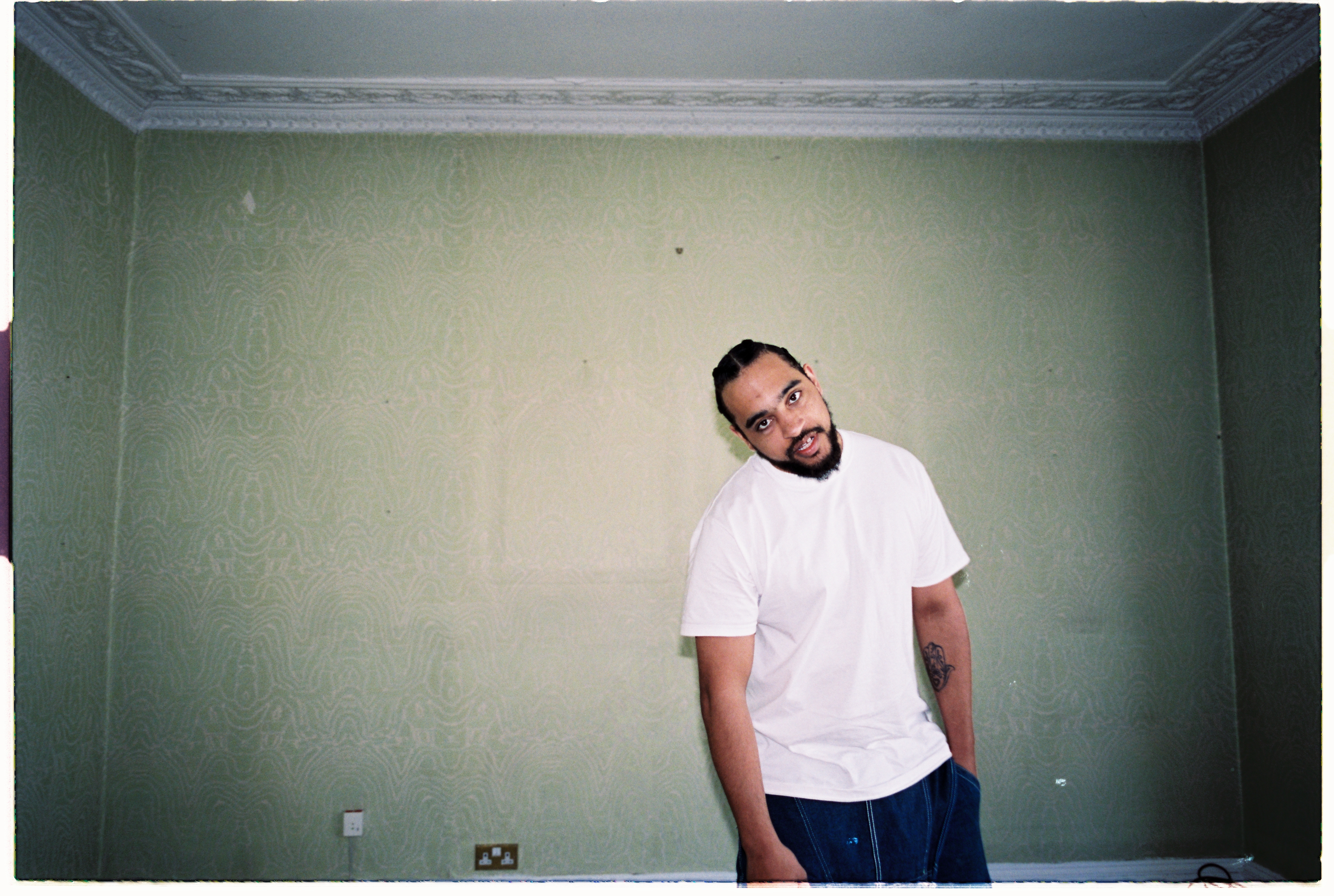 WU-Lu stood in a bare room with light green walls looking into the camera with his head cocked.