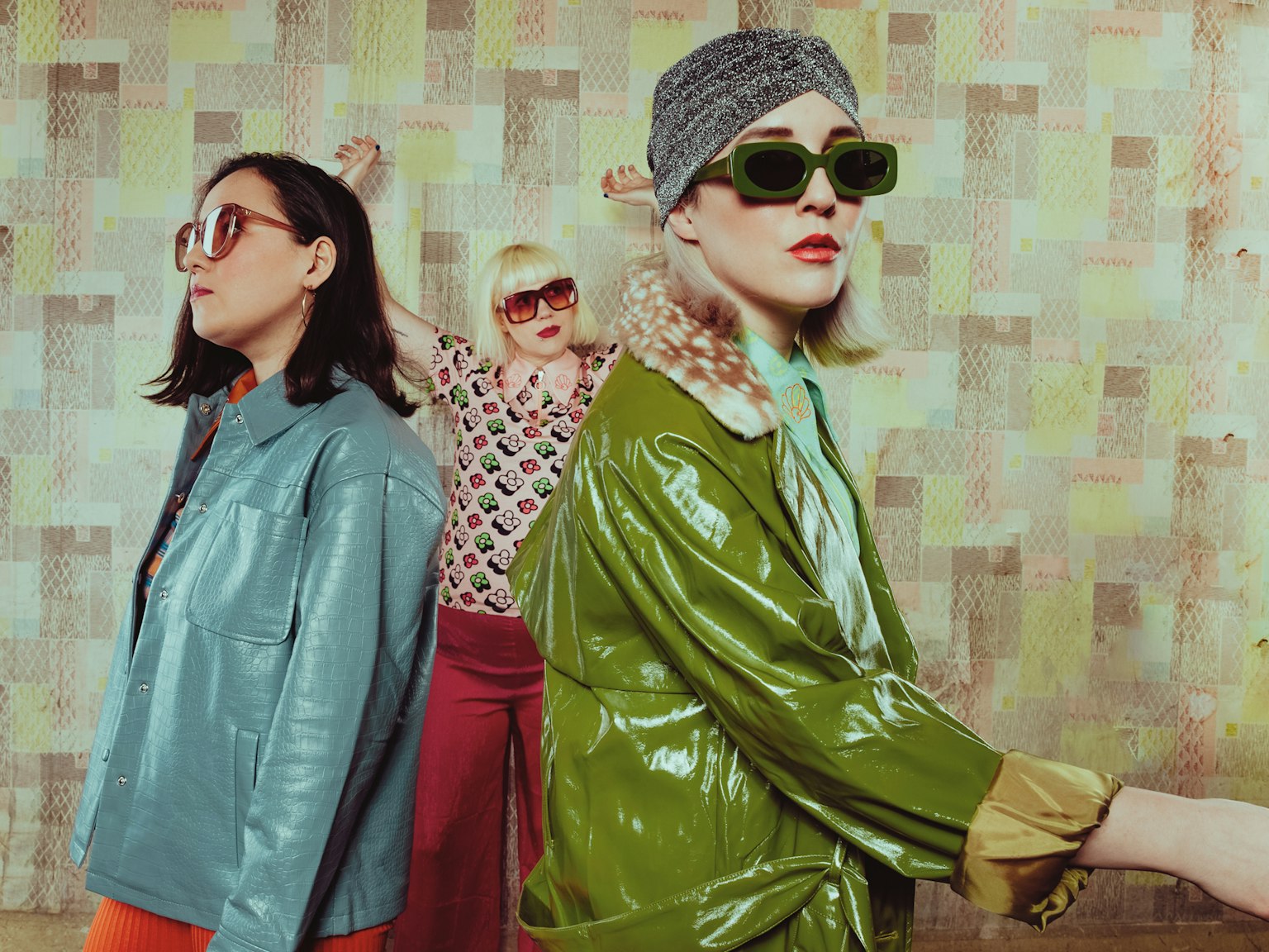 The three members of PINS wearing colourful leather jackets and shirts with big blocky sunglasses on.