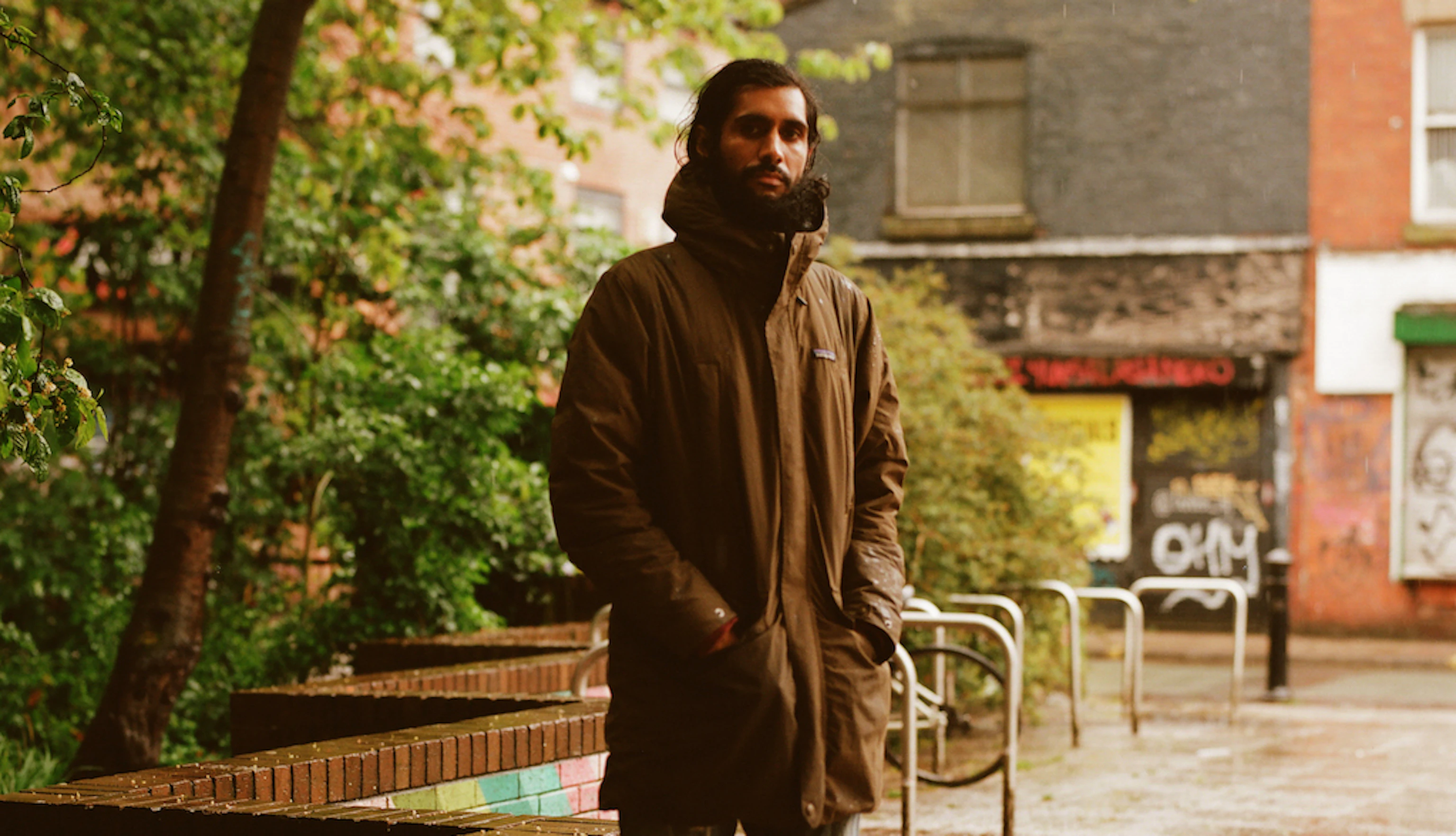Balraj Samrai stood on a pavement. He's dressed in a parka jacket with his hands in his pockets. Behind him are trees, shops and bike stands.
