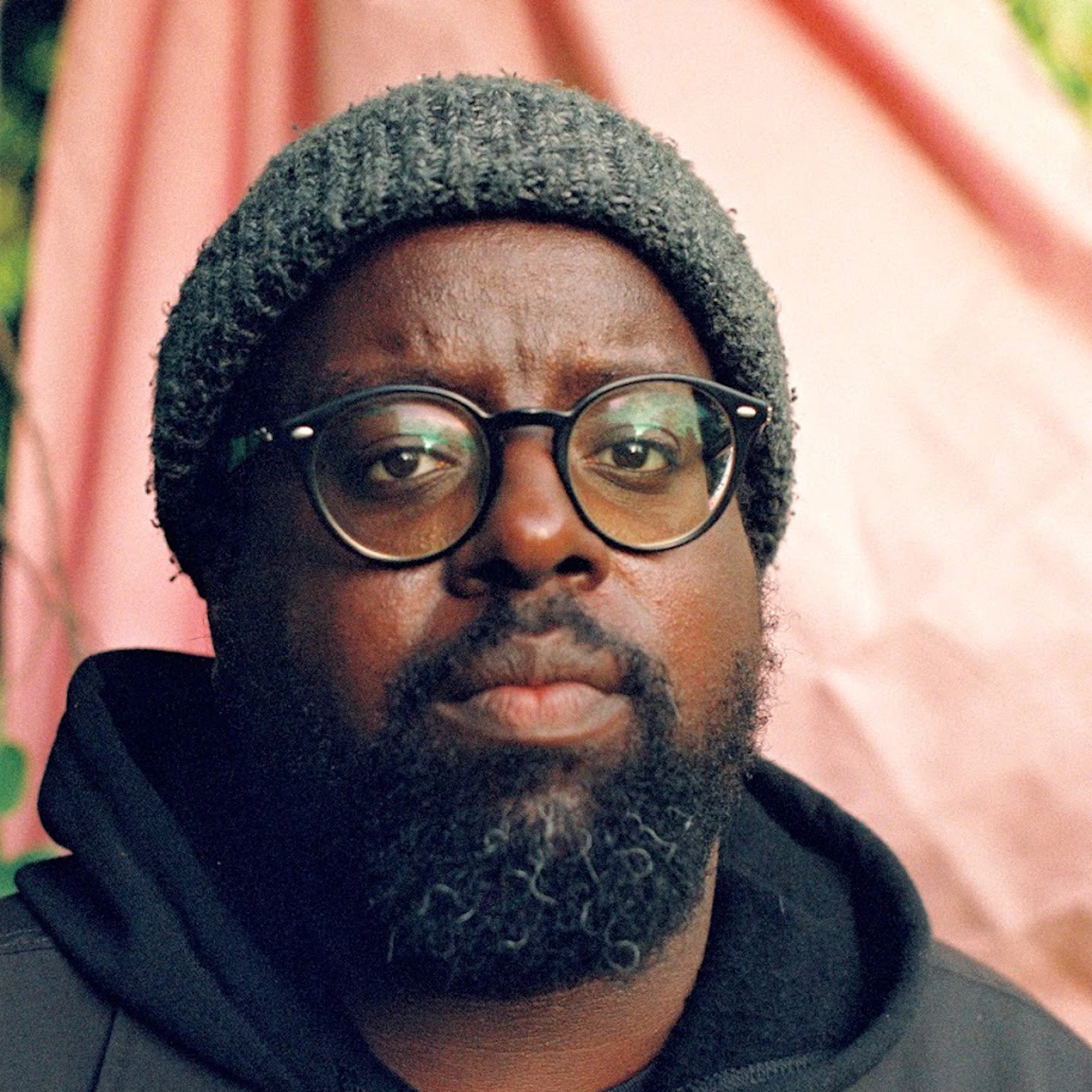 Daudi Matsiko is wearing glasses, a beanie, a hoodie and a coat looking into the camera.