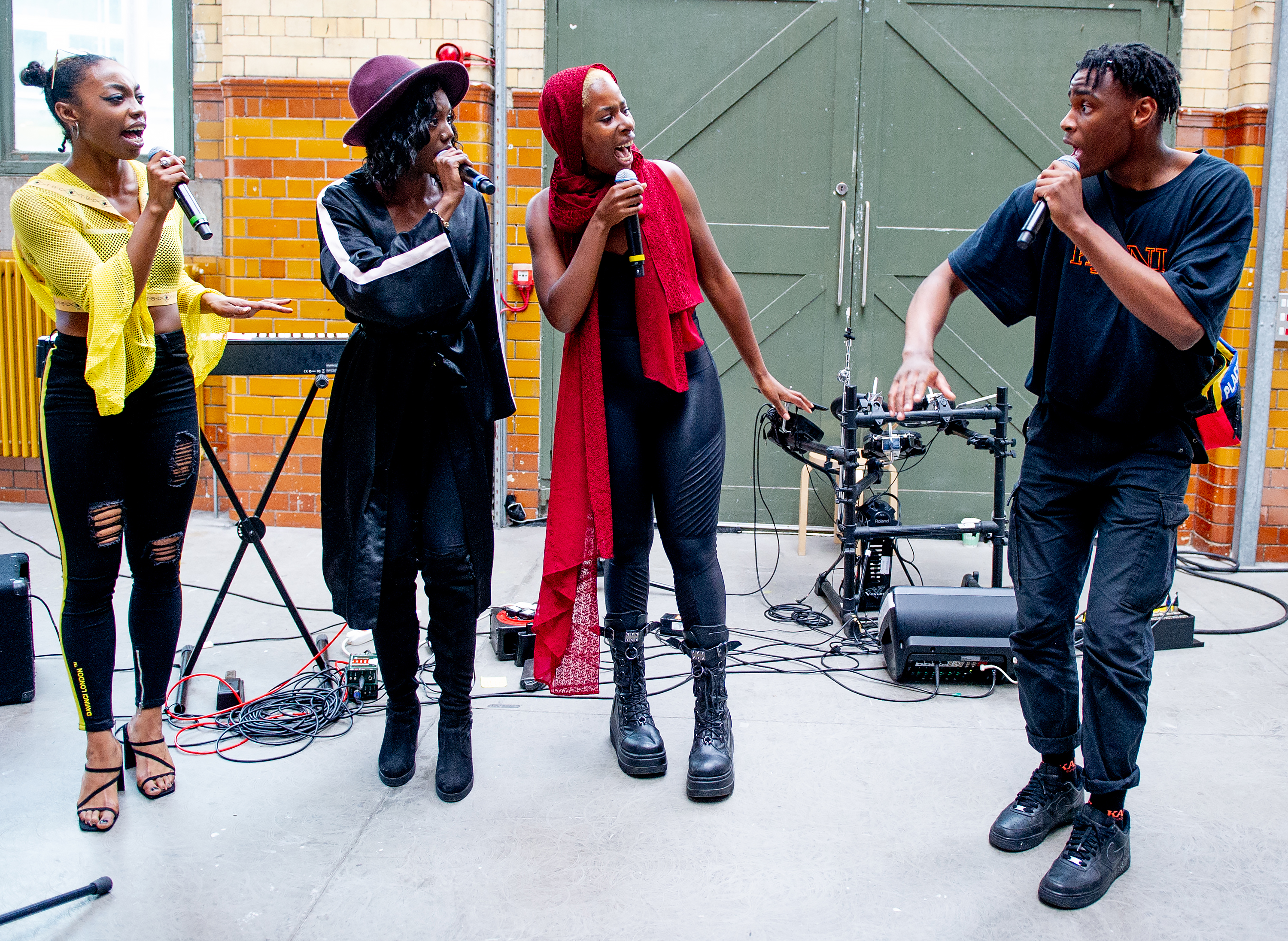 Four of the DISRUPT creative team stood in a line singing into microphones and looking at one another.