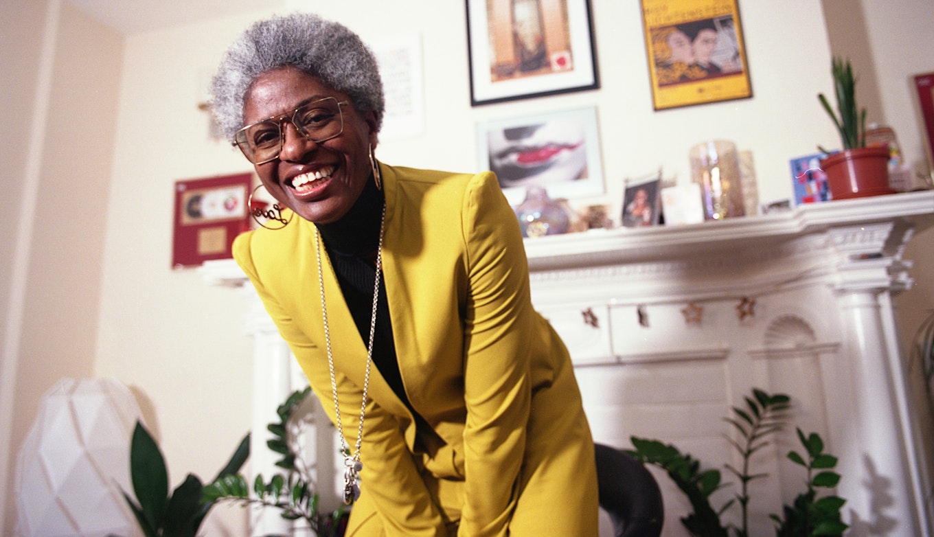 DJ Paulette wearing a yellow suit jacket and a beaming smile.