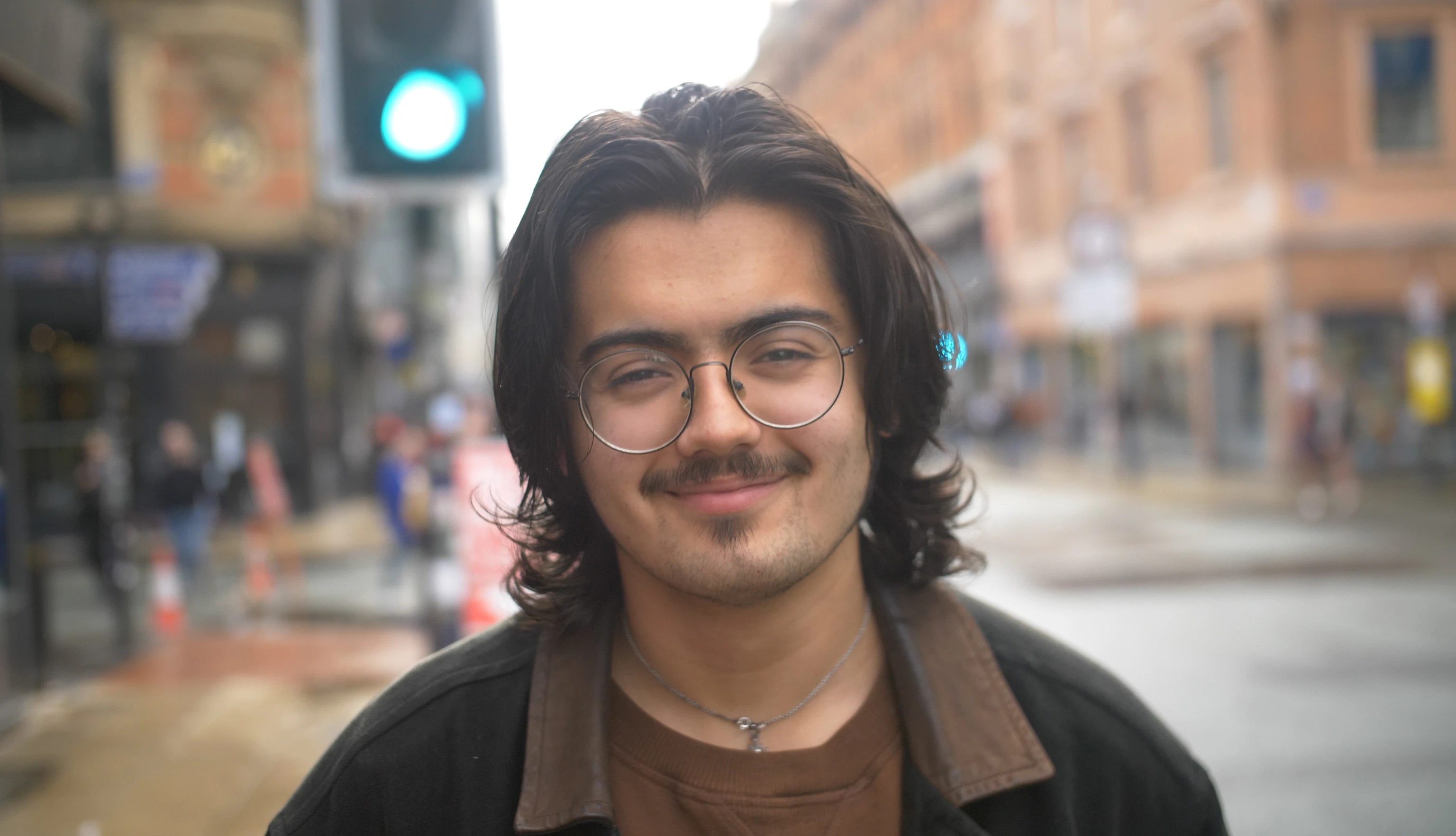 Tom Rabbani stands on a Manchester street. He is looking straight into the camera with smile.