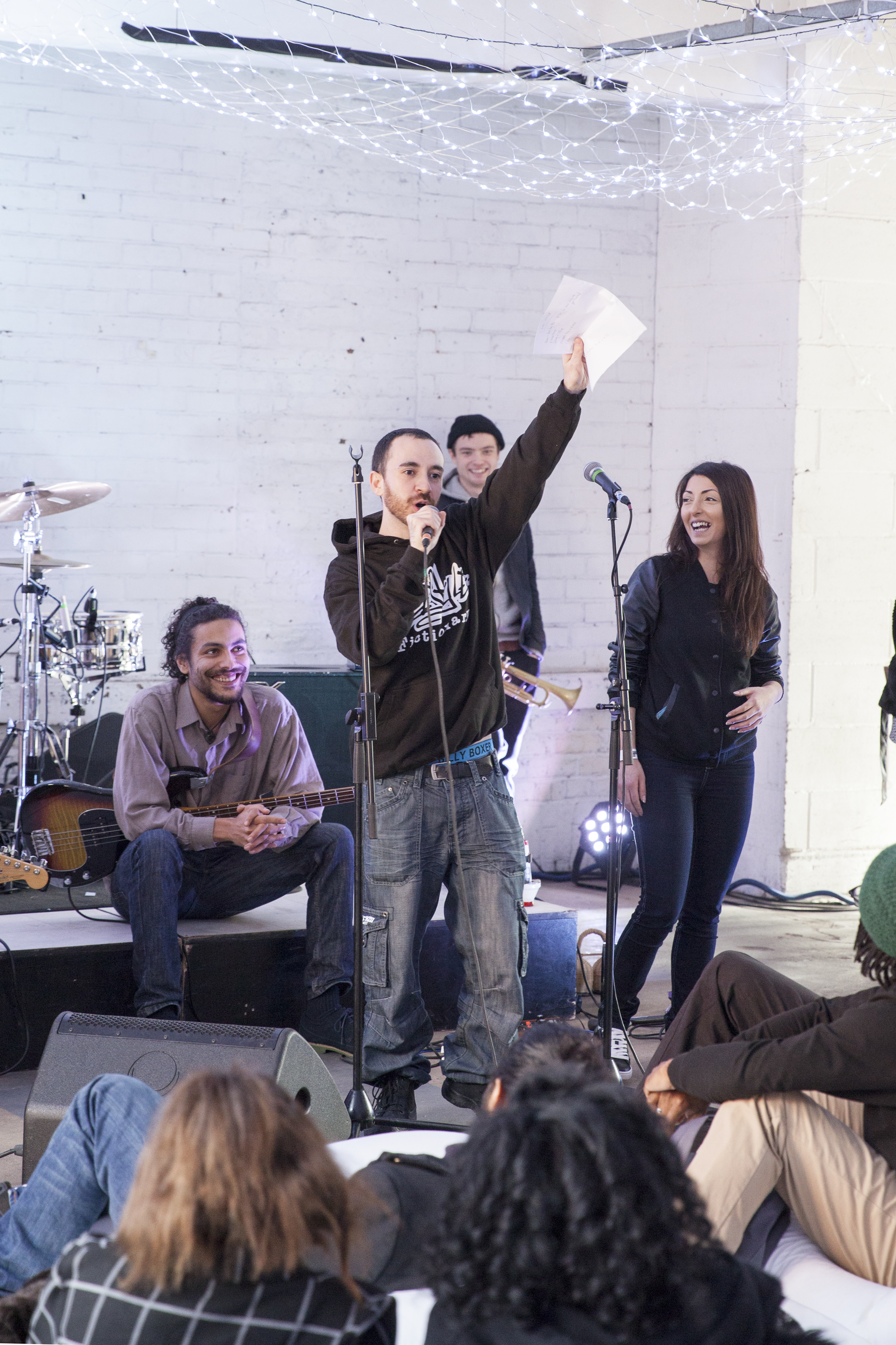 Facilitator on stage speaking into a microphone, participants and band looking at them smiling 
