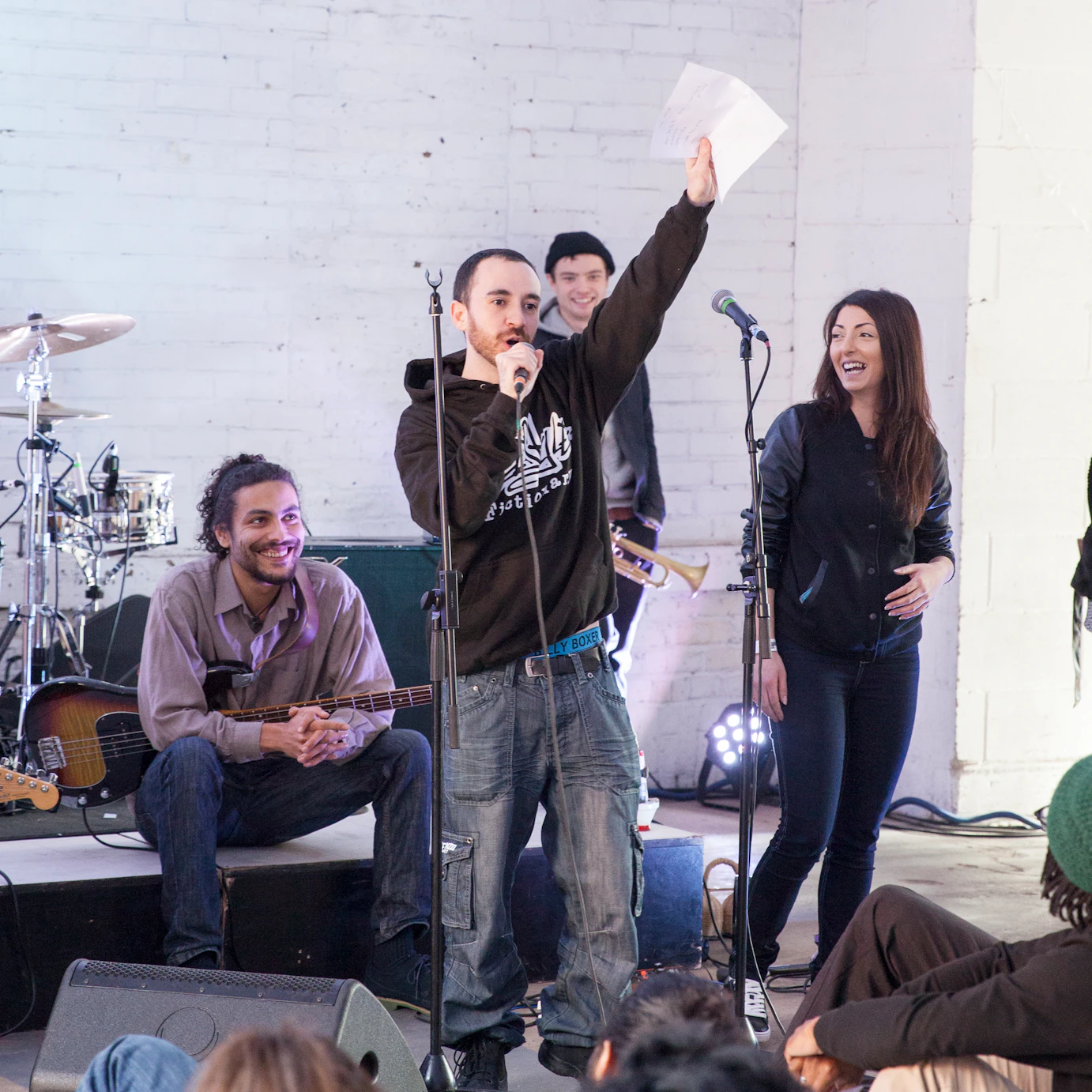 Facilitator on stage speaking into a microphone, participants and band looking at them smiling