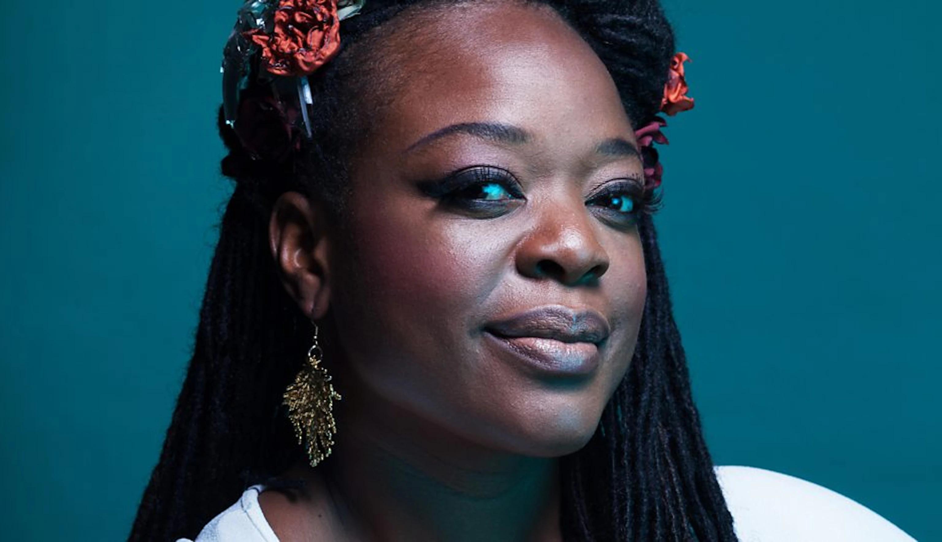 Headshot of ESKA smiling at the camera with flowers in her hair against a teal background.
