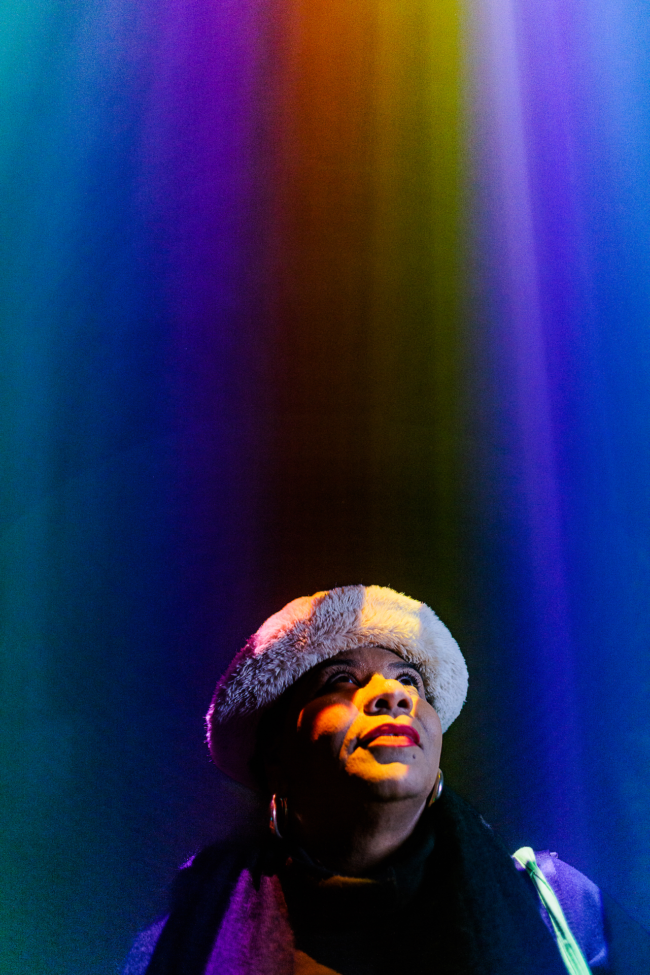 Someone looking up as projections shine down on their face in various colours including purple, blue, yellow and orange.