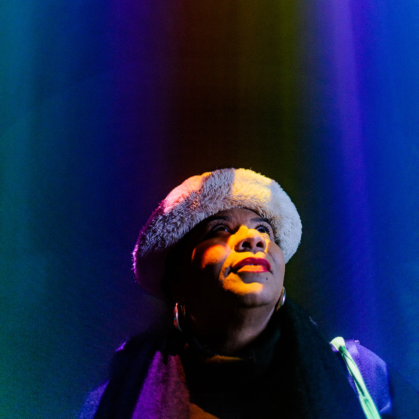 Someone looking up as projections shine down on their face in various colours including purple, blue, yellow and orange.