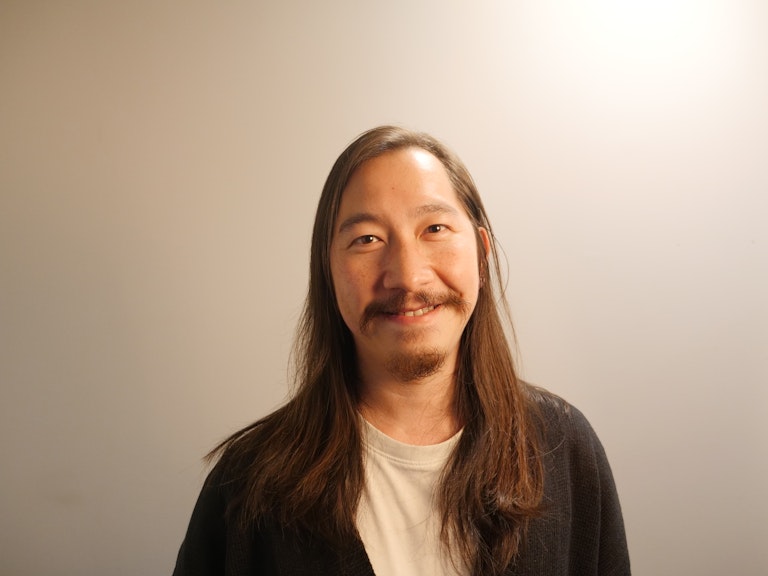 Anthony Lee smiles at the camera. He has long dark hair, a moustache and goatee beard.