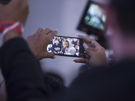 A close-up of someone's hands holding a smart phone. They are recording a group of musicians rapping with Kendrick Lamar. 