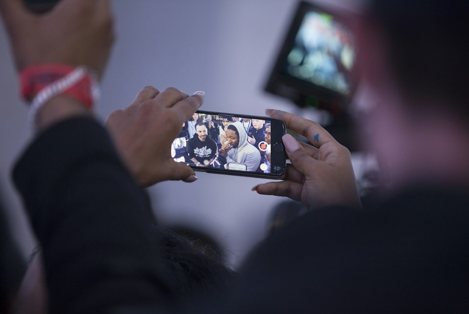 A close-up of someone's hands holding a smart phone. They are recording a group of musicians rapping with Kendrick Lamar.
