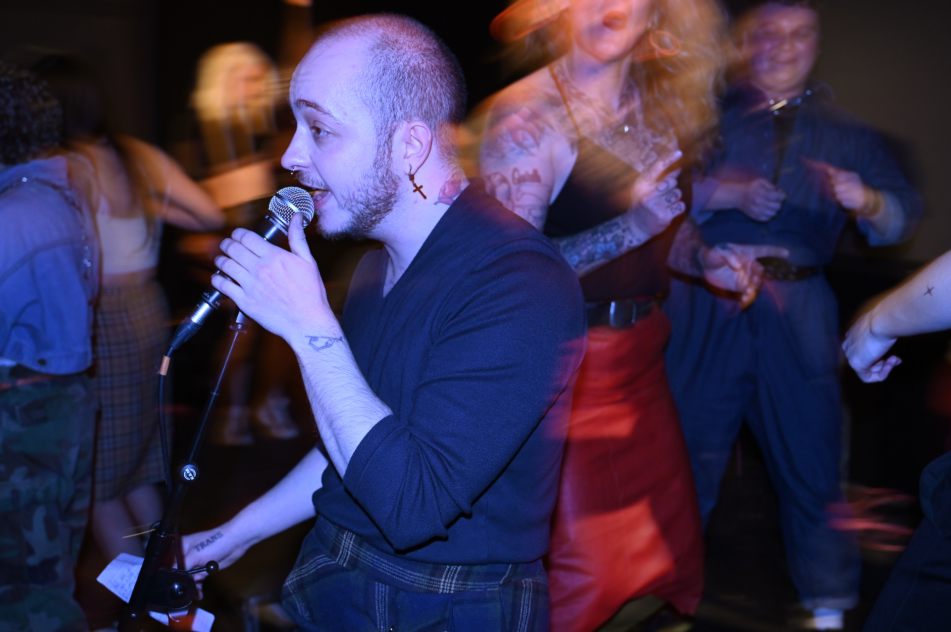 A residency artist with a mic to their lips. Around them the crowd is blurred.