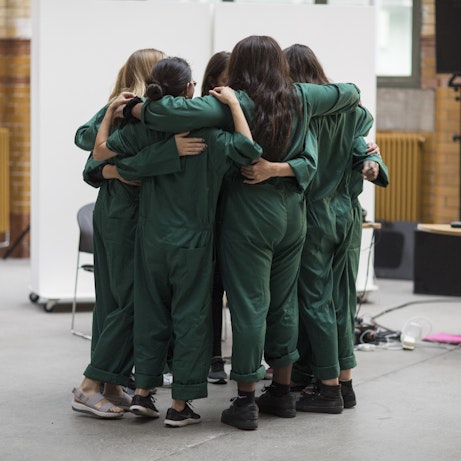 Residency artists dressed in dark green boiler suits holding one another in a group hug.