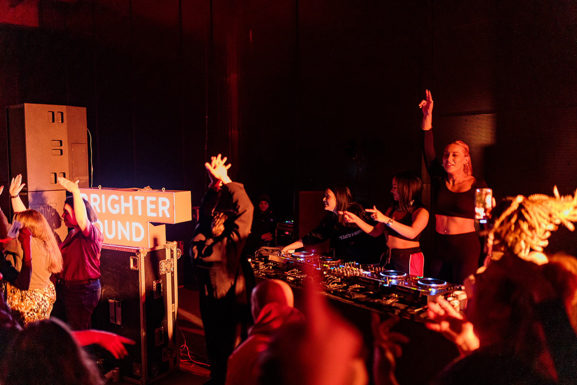 DJ collective Girls Don't Sync on the decks interacting with the crowd with hands in the air and pointing towards the audience who are dancing.