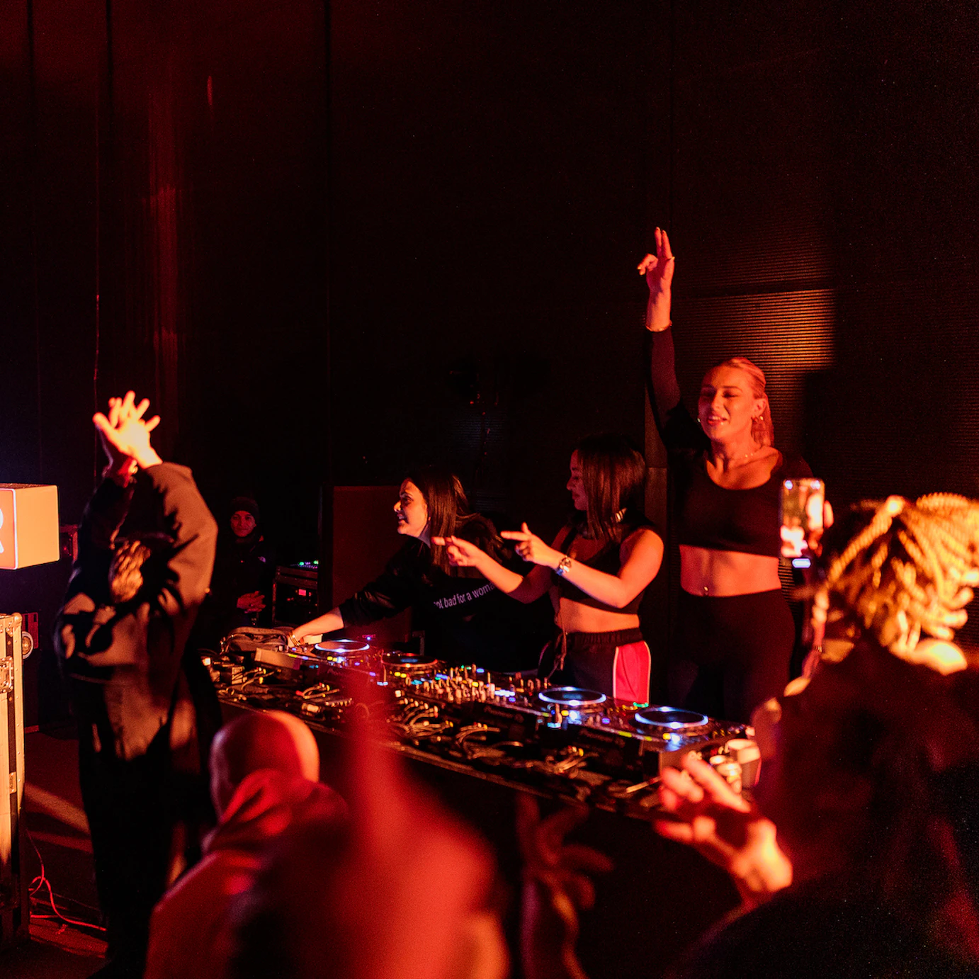 DJ collective Girls Don't Sync on the decks interacting with the crowd with hands in the air and pointing towards the audience who are dancing.