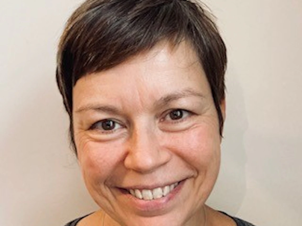 Jo Harvie smiles broadly into the camera. She has short dark hair.