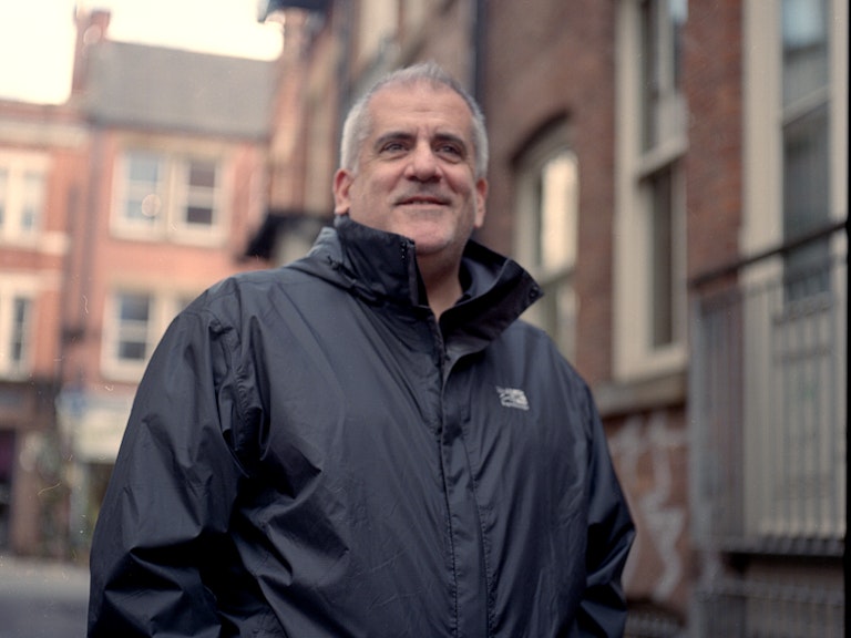 Gareth is wearing a black coat and smiles beyond the camera. 