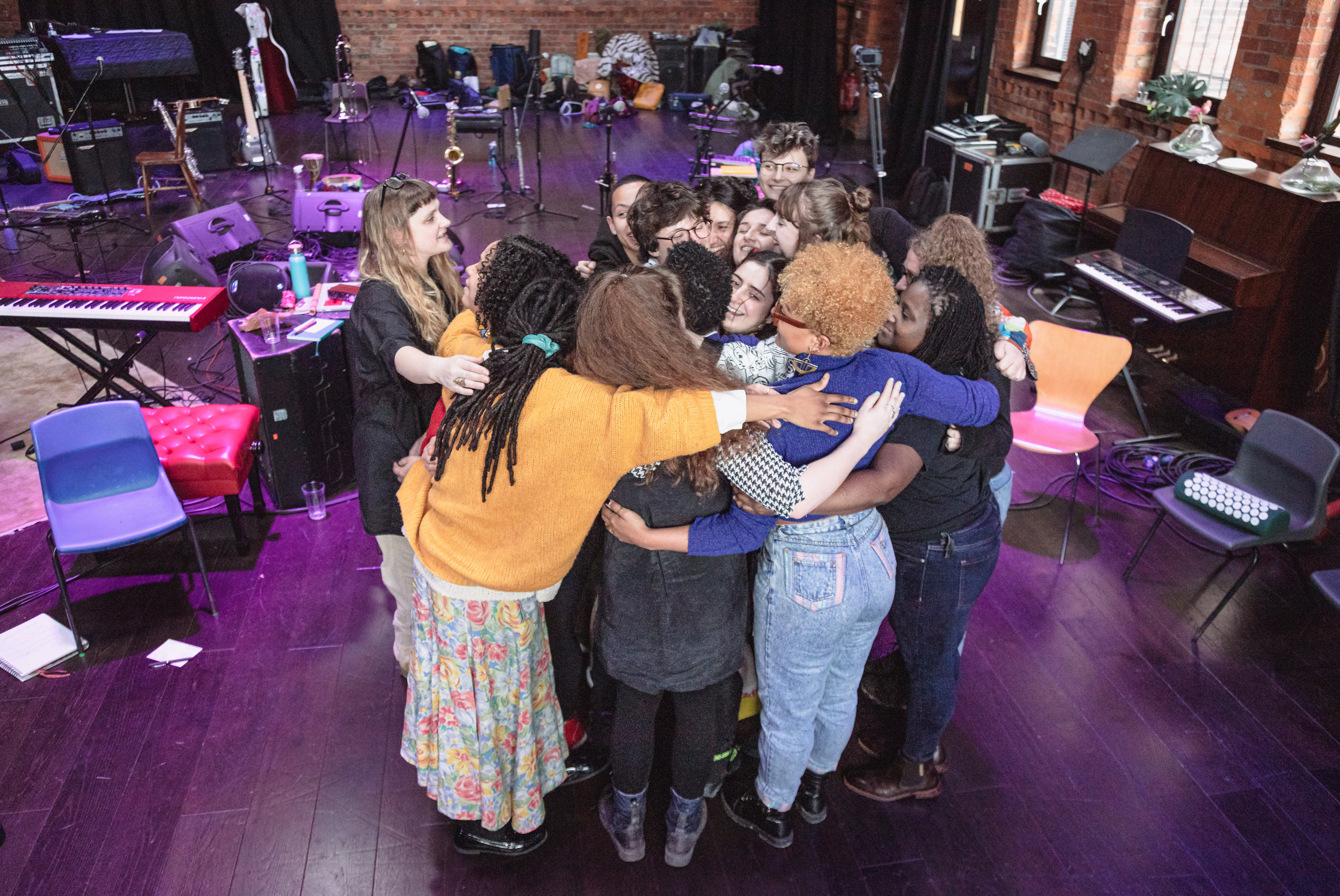 A group of musicians all in a big group hug amidst musical equipment and instruments.
