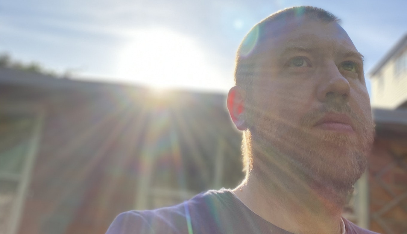 A close up of whiskas looking up outside on a street. Sun rays bleed into the shot as they encroach over the roof of a building behind whiskas.