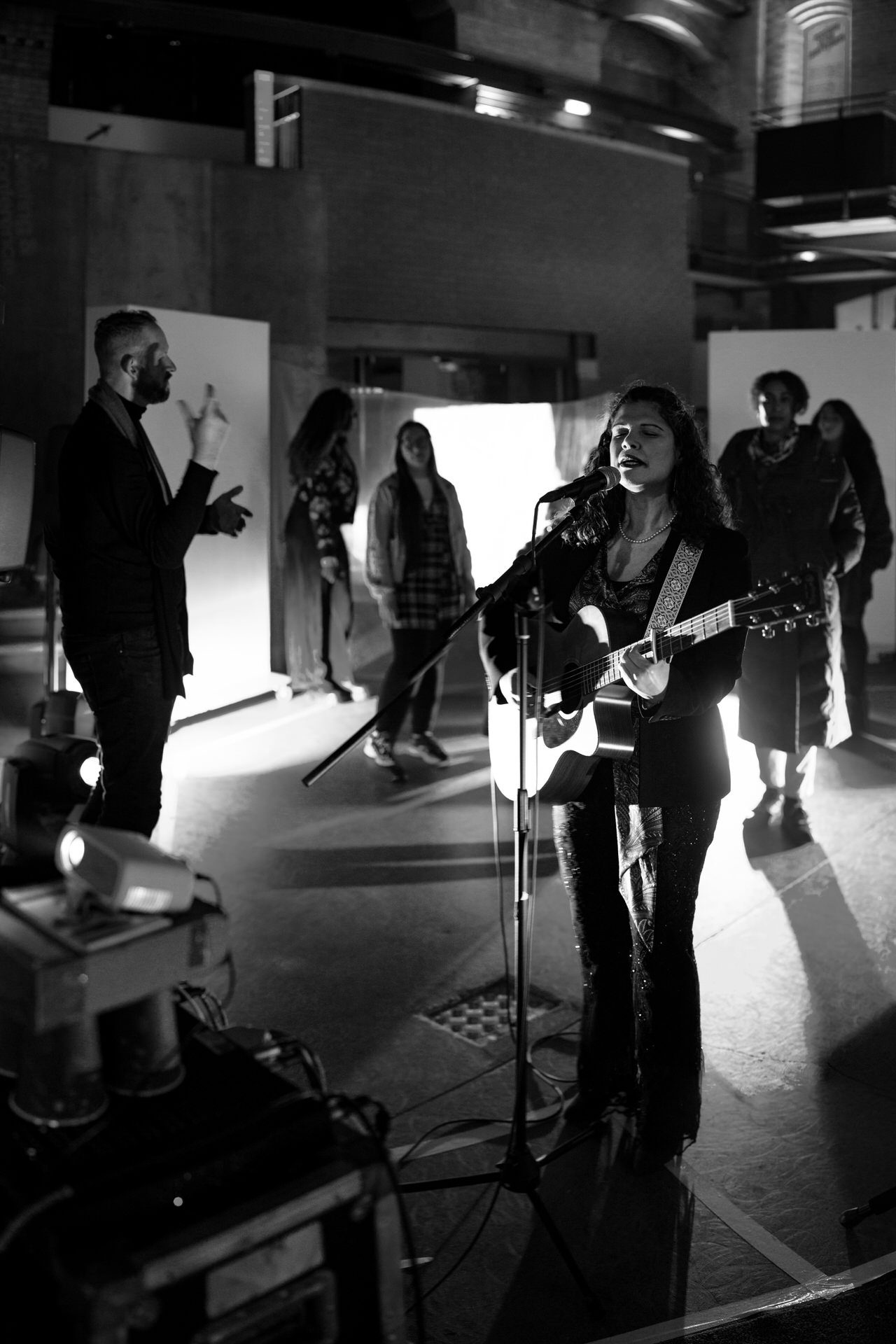 Elena Piras performing with an acoustic guitar as part of the Self, Sense, Space installation. Audience members are gathered around her.