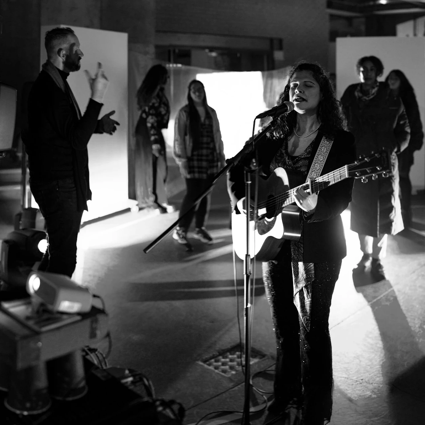 Elena Piras performing with an acoustic guitar as part of the Self, Sense, Space installation. Audience members are gathered around her.