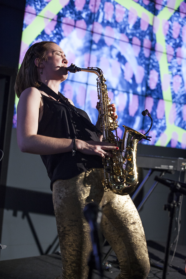 A musician playing saxophone in front of projected visuals.