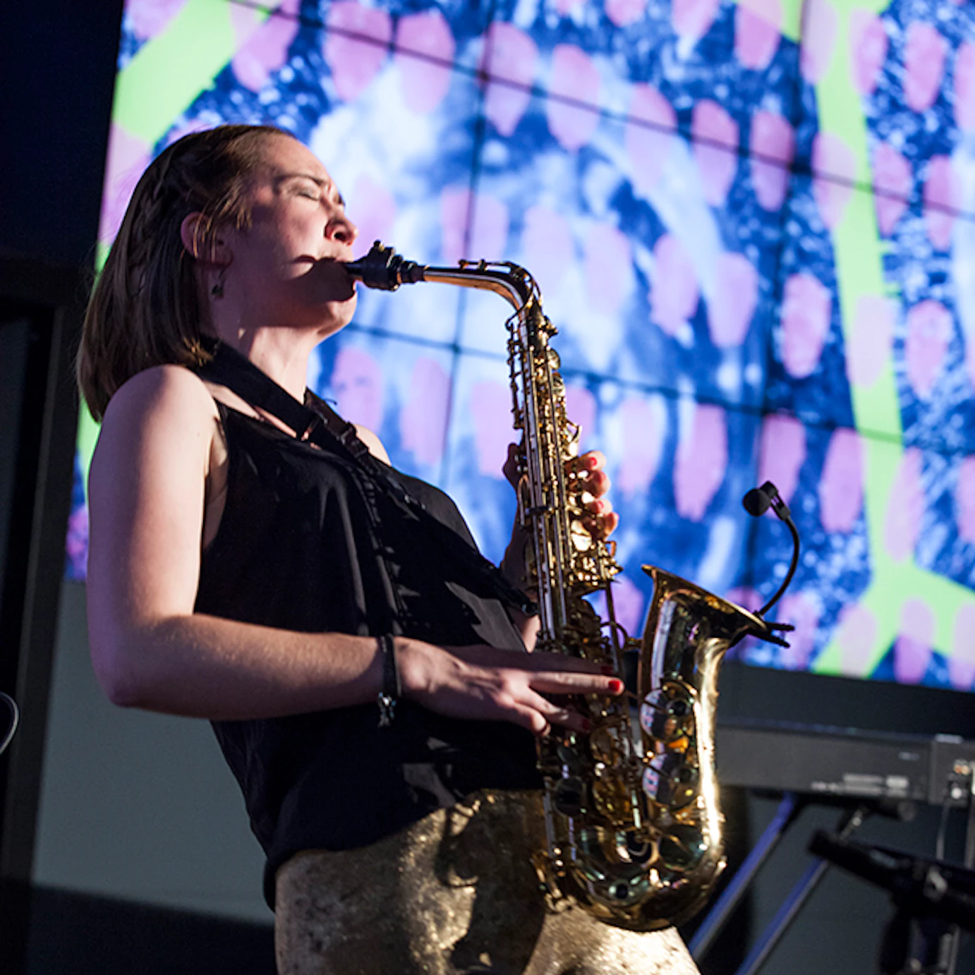 A musician playing saxophone in front of projected visuals.