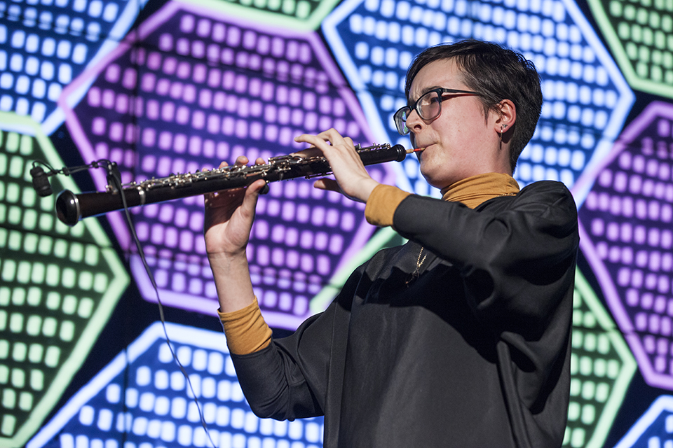A musician playing clarinet in front of projected visuals.