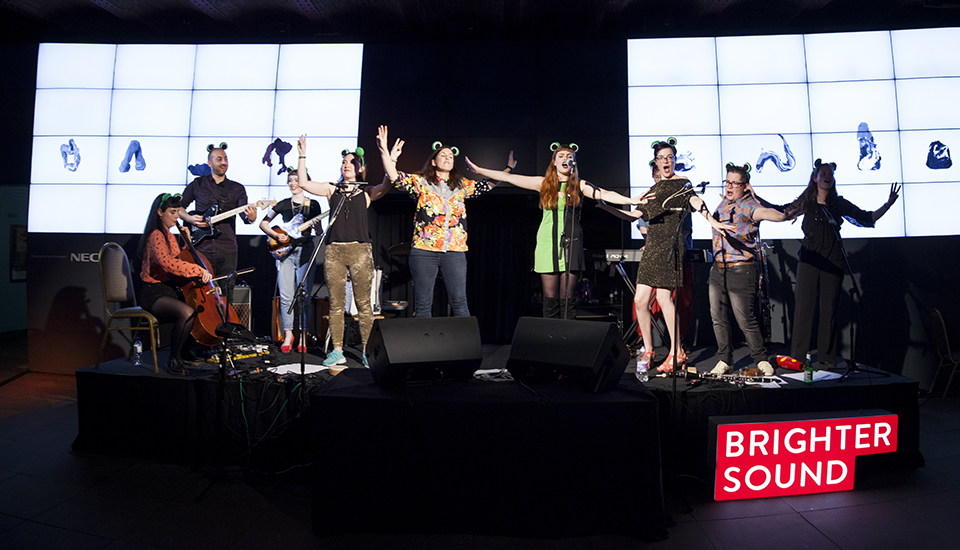 Musicians singing on stage with Anna Meredith while wearing frog ears.