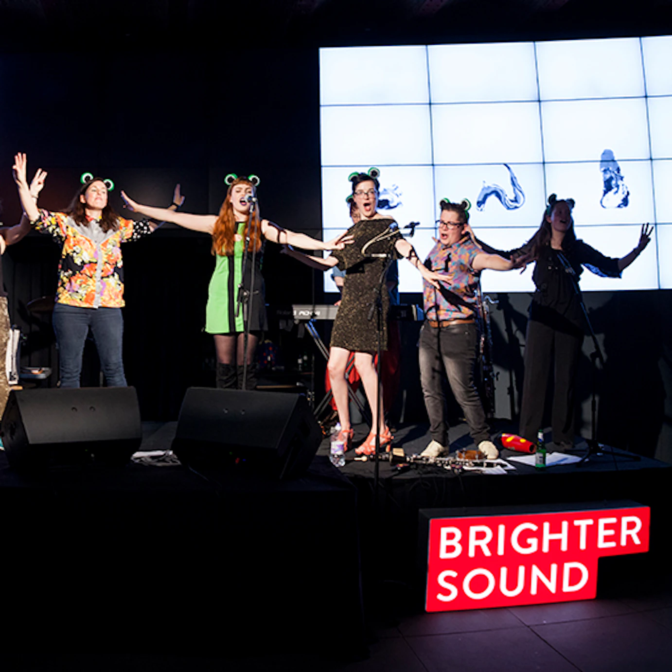 Musicians singing on stage with Anna Meredith while wearing frog ears.