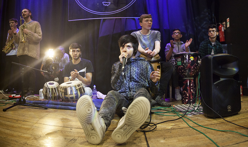 A singer sat on stage surrounded by other musicians.