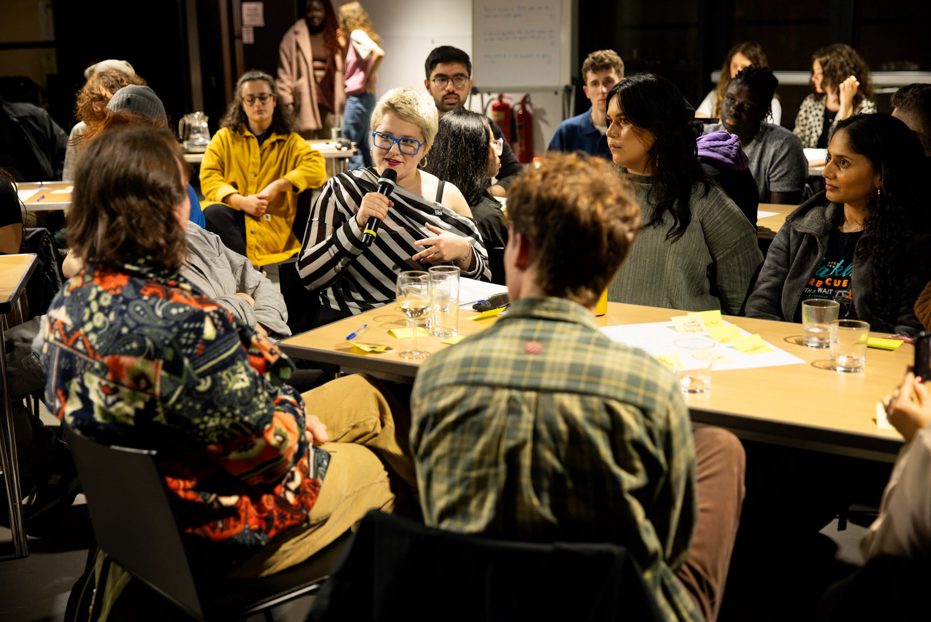 Someone speaking into a microphone sat at a table surrounded by others who are listening.