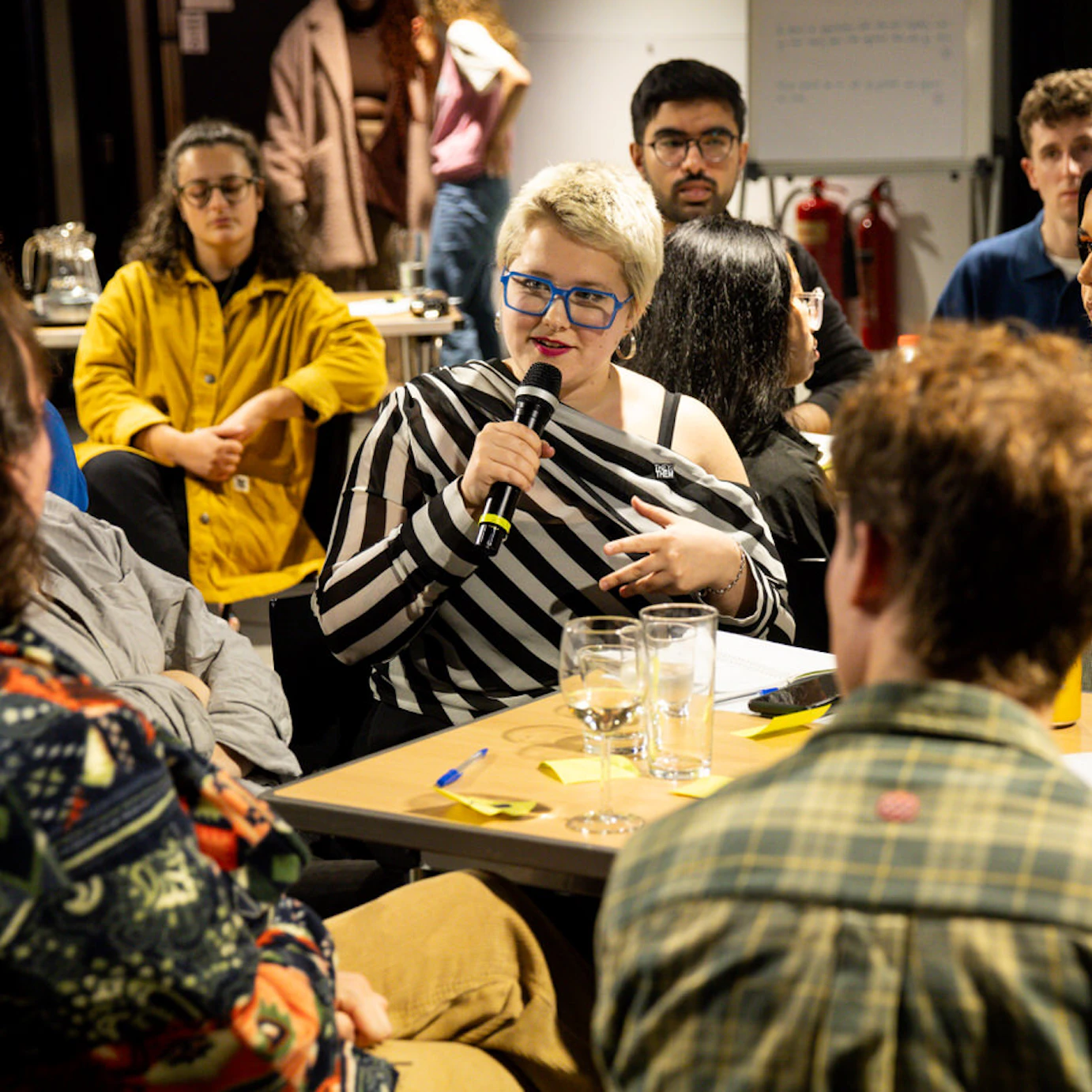 Someone speaking into a microphone sat at a table surrounded by others who are listening.