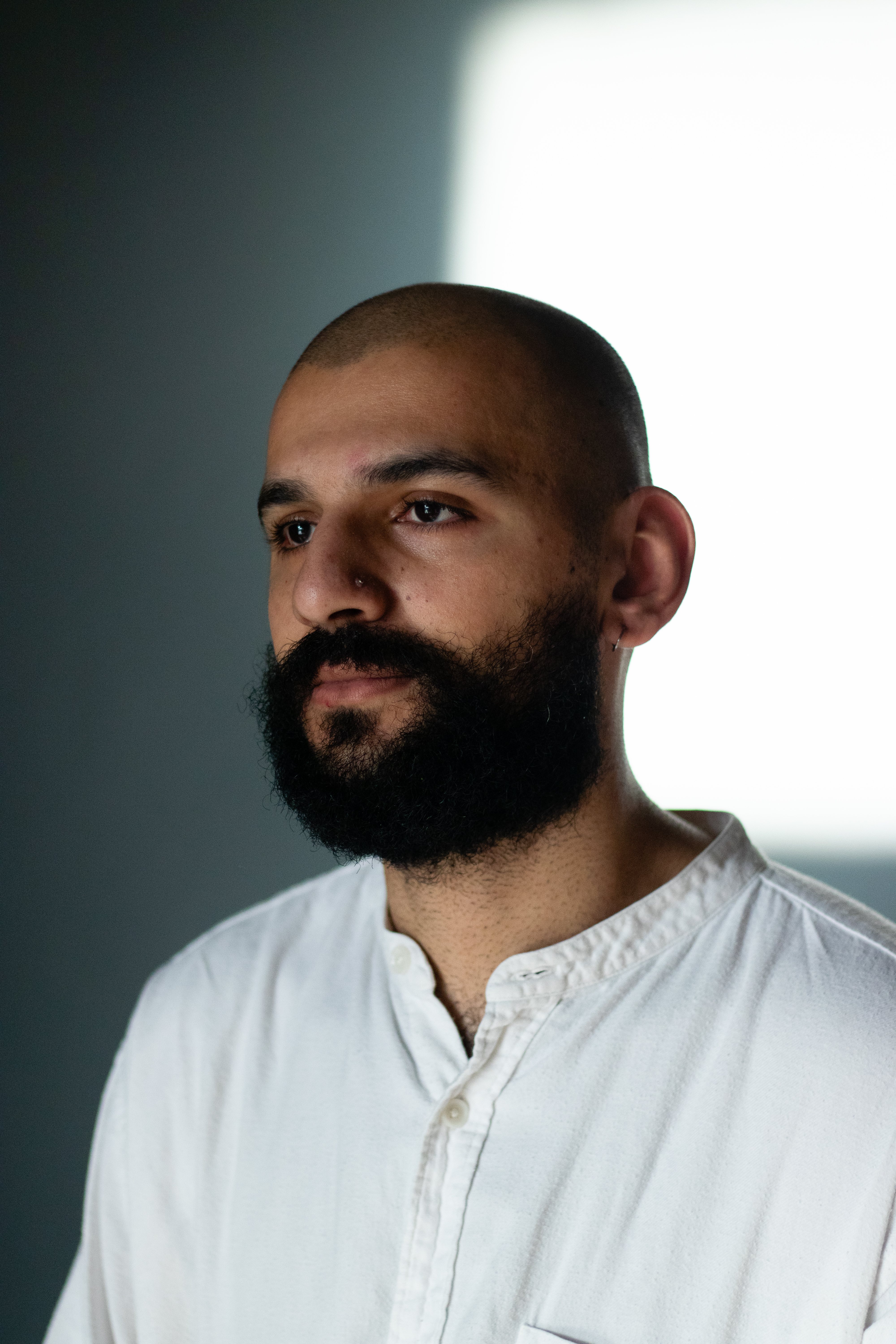Raheel Khan looking into the distance. The background white wall is half cast in shadow.