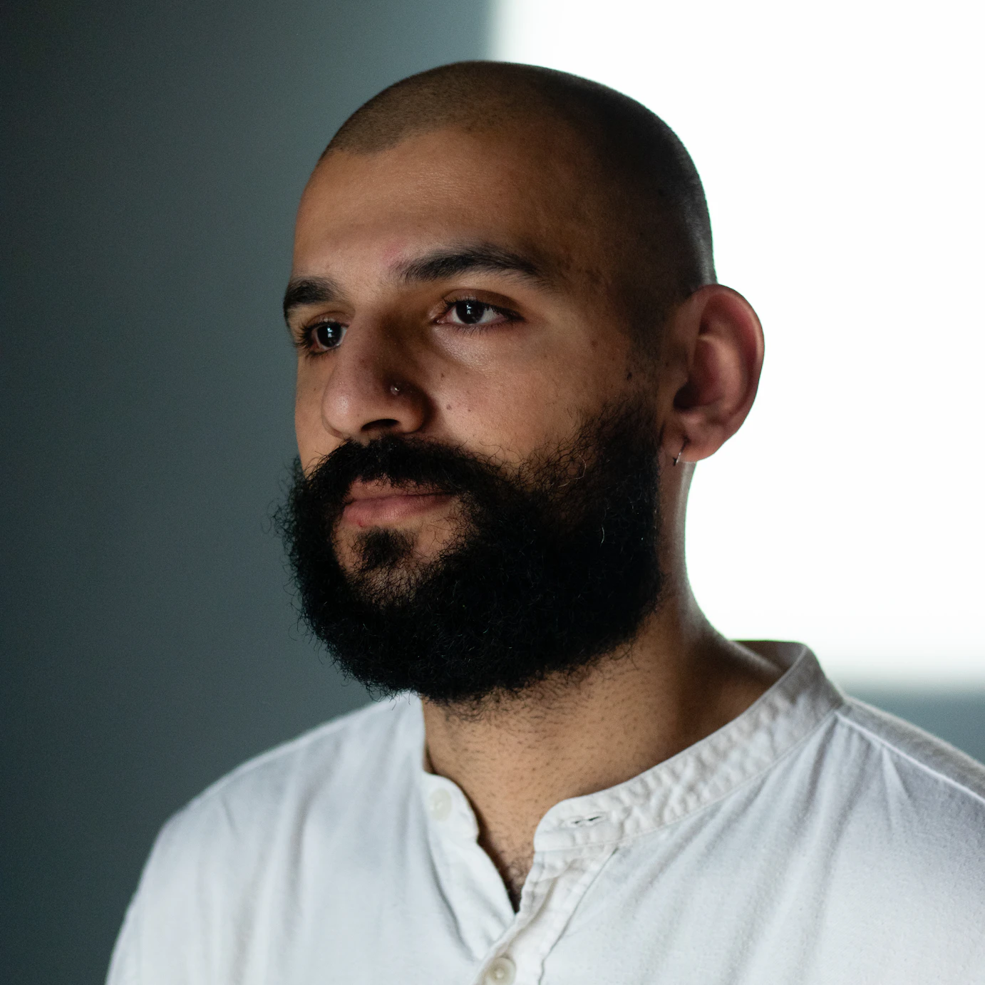 Raheel Khan looking into the distance. The background white wall is half cast in shadow.