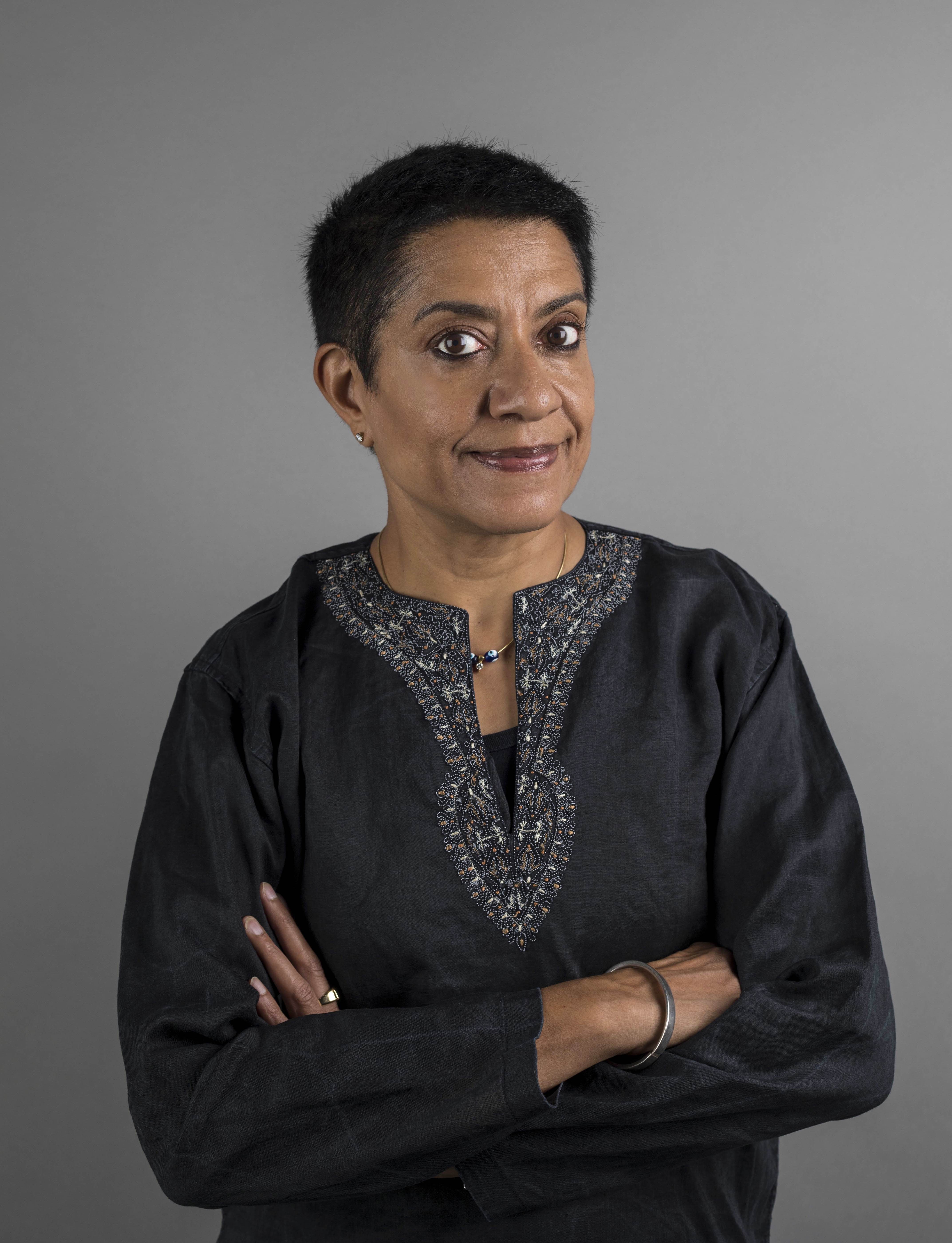 DJ Ritu on a grey background with her arms folded.