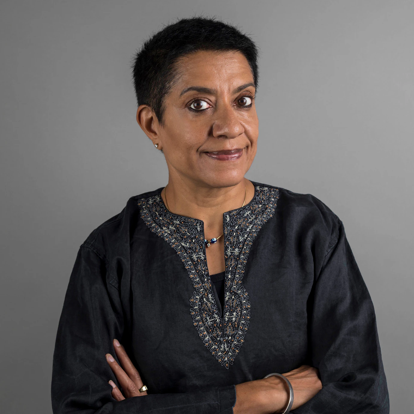 DJ Ritu on a grey background with her arms folded.